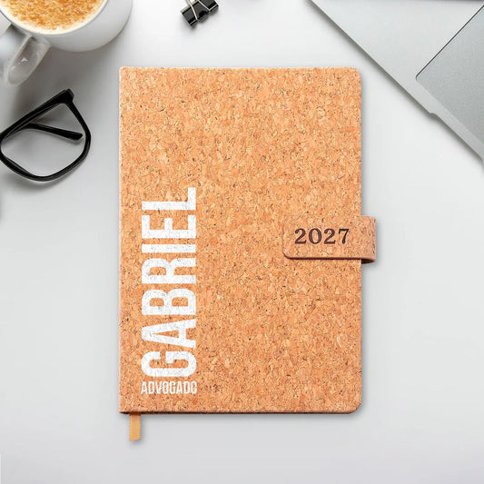 Agenda diária 2027 personalizada com nome e profissão. Capa em cortiça com fecho magnético, formato A5.