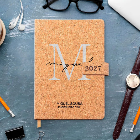 Agenda diária 2027 personalizada com nome e profissão. Capa em cortiça com fecho magnético, formato A5.