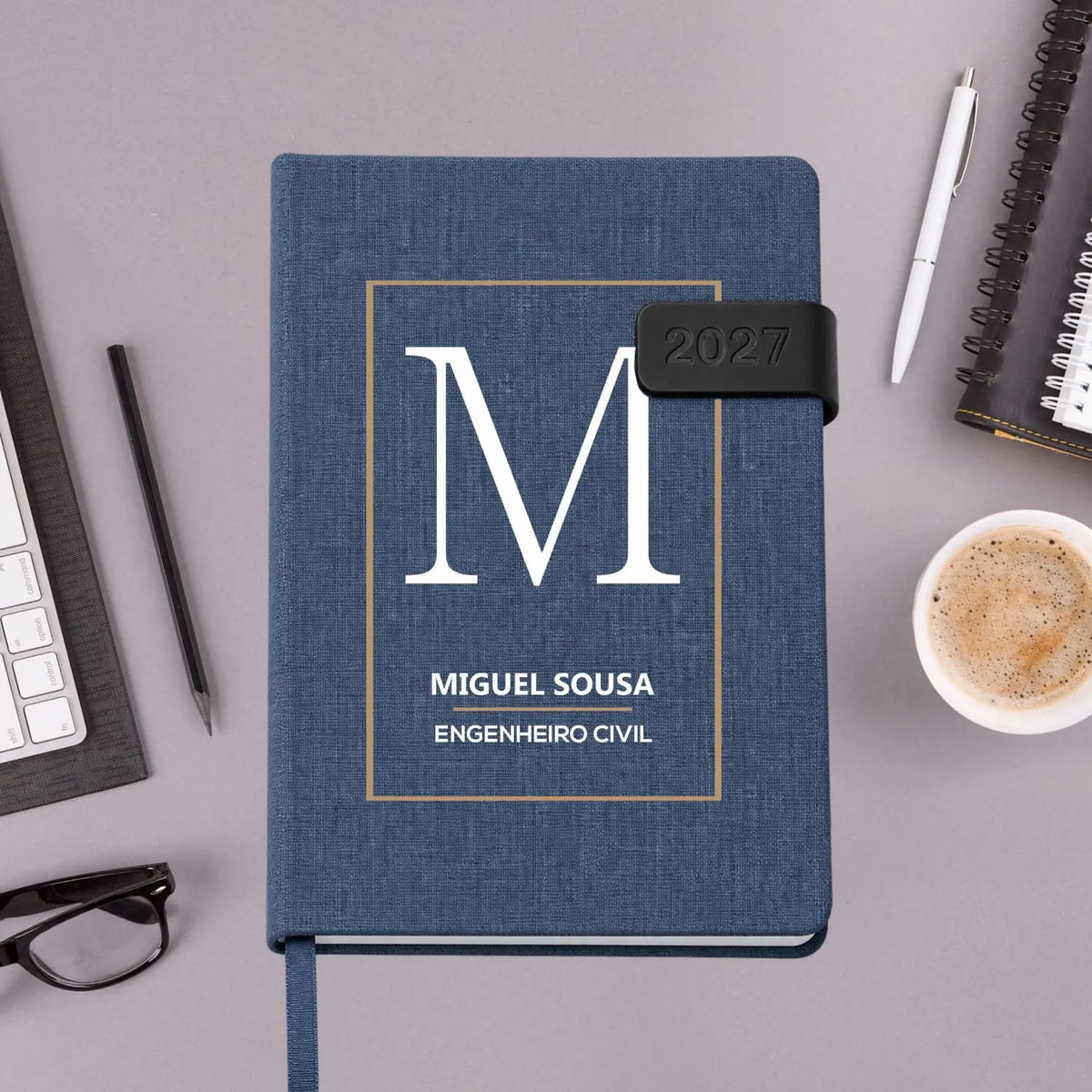 Agenda diária 2027 personalizada com nome e profissão. Capa em tecido com fecho magnético, formato A5.