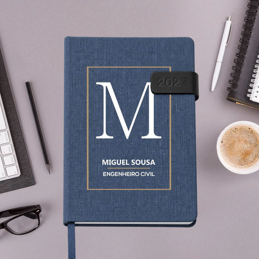 Agenda diária 2027 personalizada com nome e profissão. Capa em tecido com fecho magnético, formato A5.