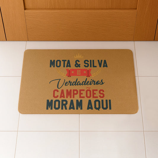 Tapete de entrada personalizado com apelido(s) da família. Superfície de fibra sintética. Base de borracha preta antiderrapante. 40x60 cm.